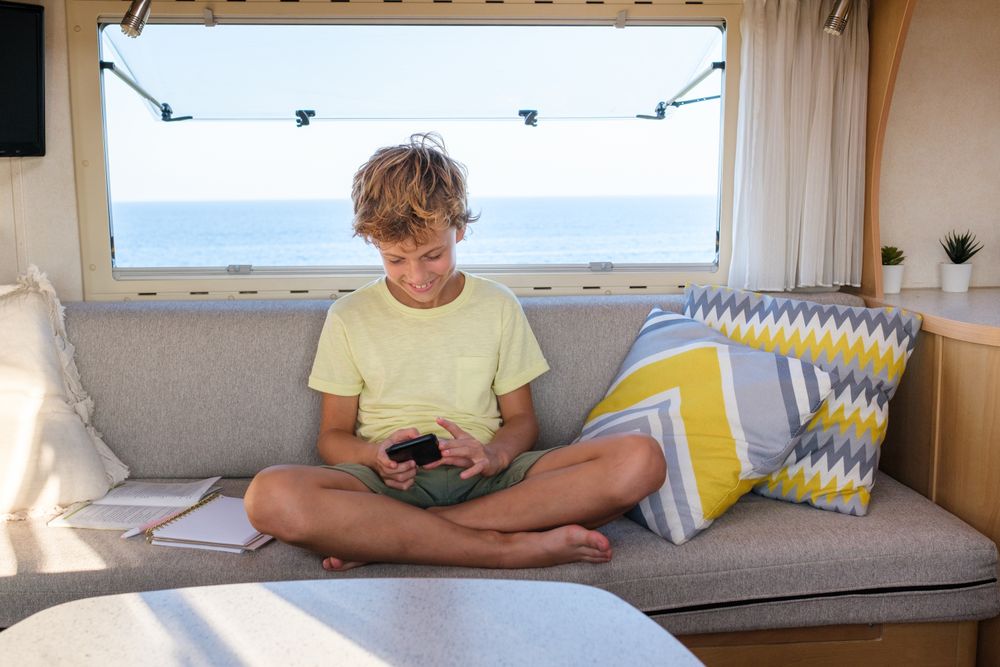 Optimistic boy using mobile phone on caravan couch
