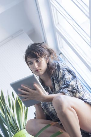 Female in flannel shirt lounging at home with digital tablet