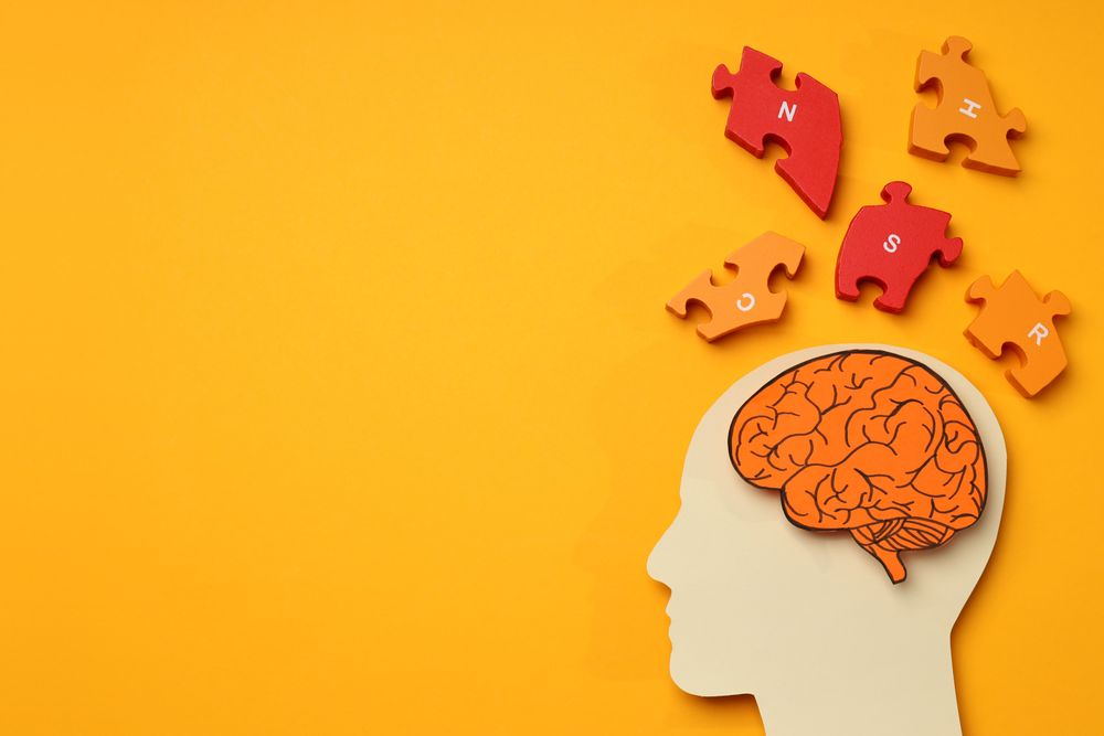 Cut out of head with brain & puzzle pieces on orange background, copy space