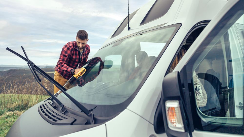 Man in checkered red shirt cleaning van’s front window with windshield wiper’s up