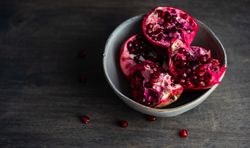 Ceramic bowl of open pomegranates on wooden table