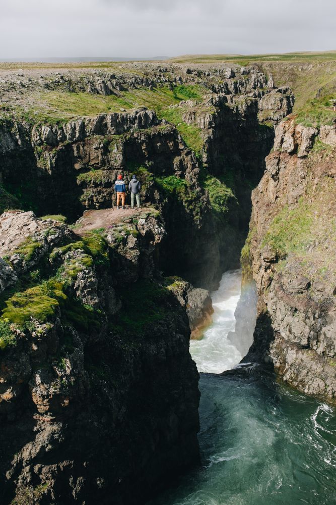 Two men on edge of cliff over waterfall, portrait