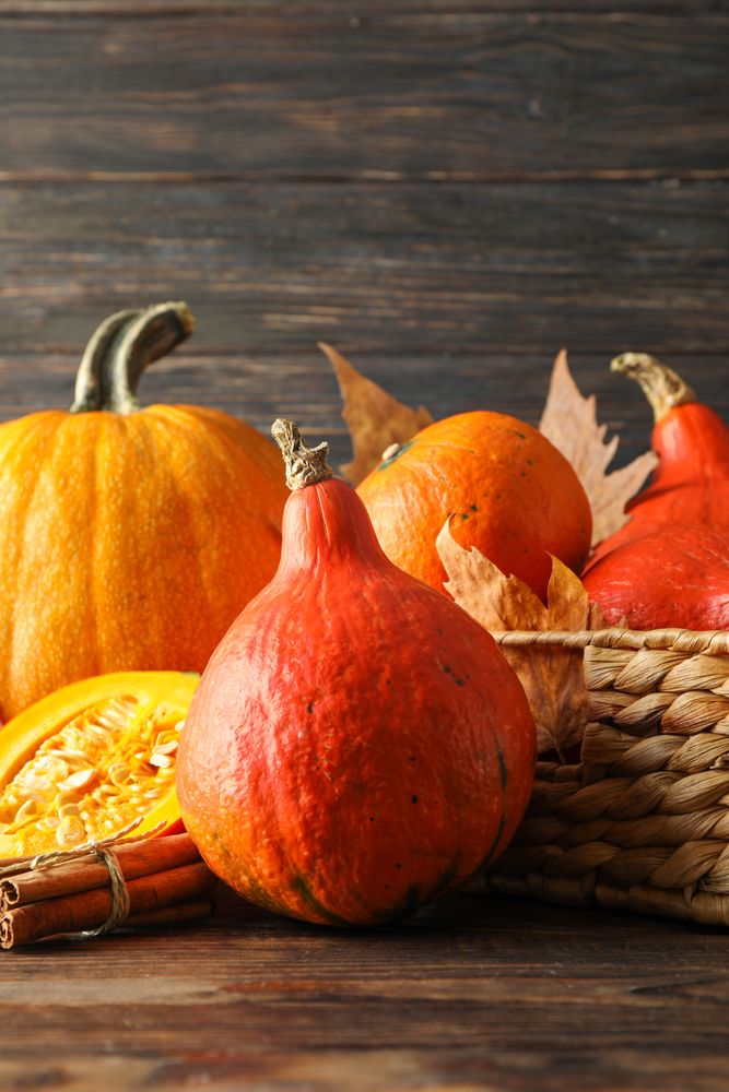 Pumpkins in straw basket on wooden background, copy space