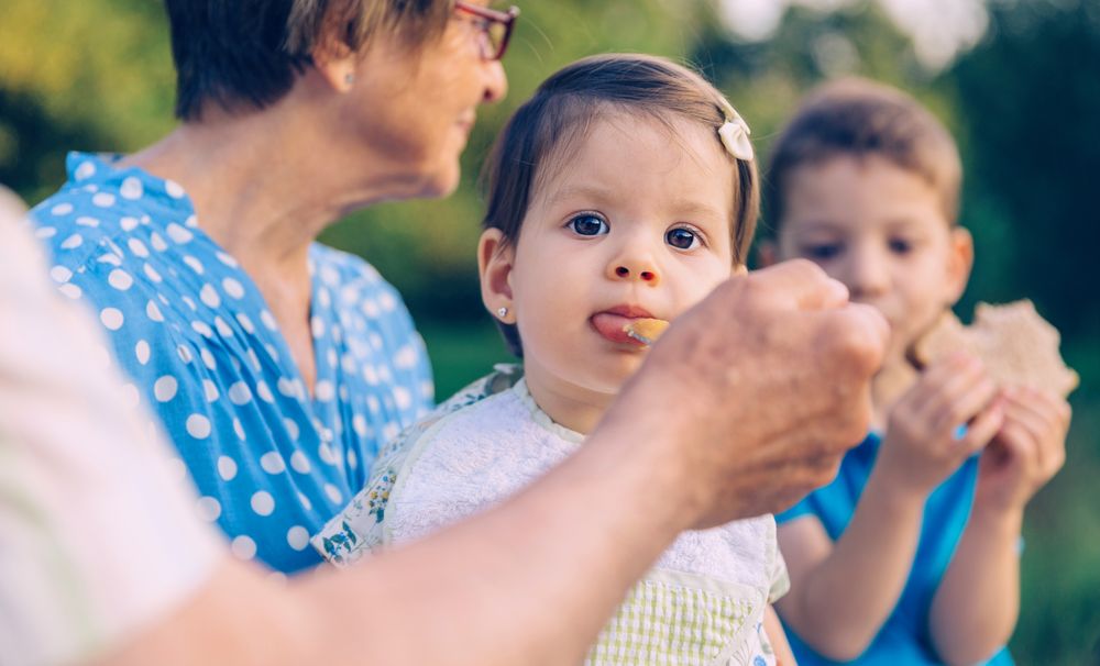 Senior man feeding to baby girl sitting on a bench
