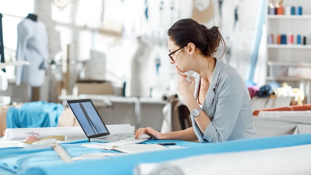 Woman fashion, designer,  Sitting at Her Desk Looking at Sketches on a Laptop, Taking Notes.