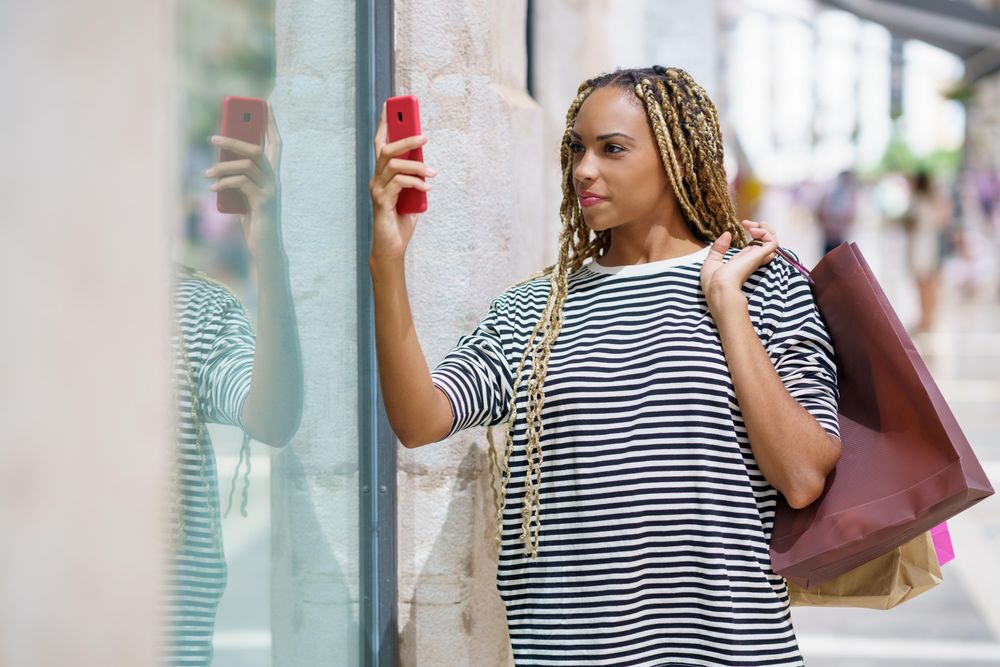 Female holding bags over her shoulder taking picture through shop window