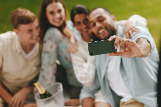 Focus on man’s hand holding smart phone to take selfie with friends