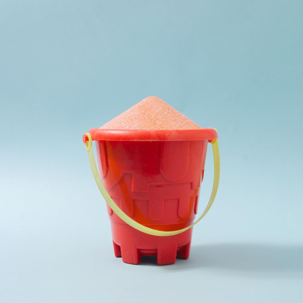 Sand castle bucket with spilled sand against pastel blue background
