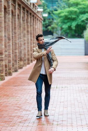 Portrait of confident young man with camel coat and tossing scarf across this shoulder while walking down street
