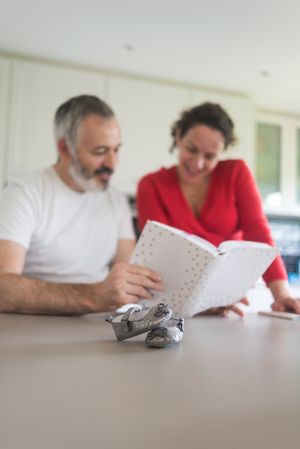 Couple looking reminiscently through book in kitchen with baby shoes in foreground
