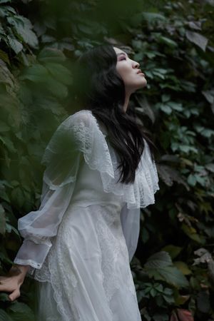 Woman in long light dress standing beside tree