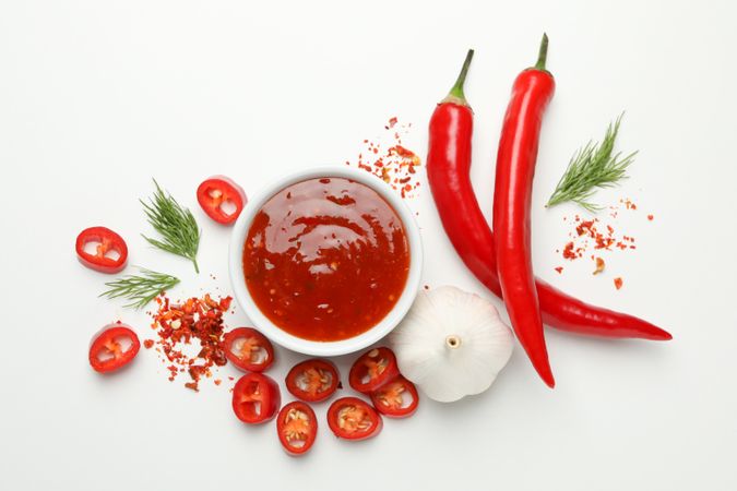 Bowl with chilli sauce, pepper and garlic on blank background