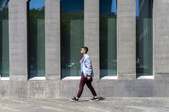 Side view of trendy man walking in the sun outside of building