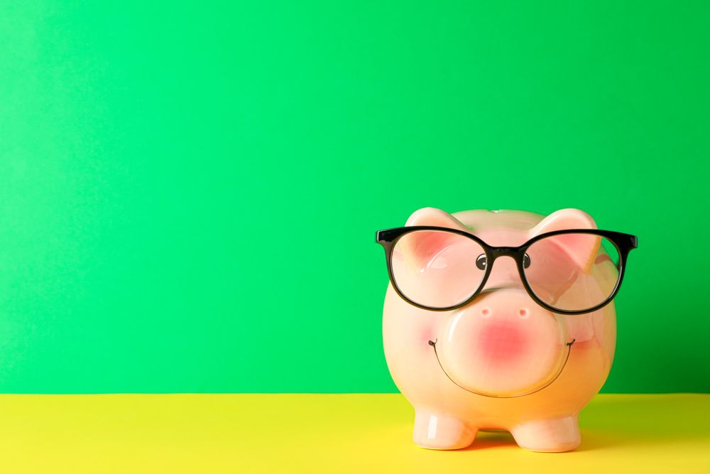 Happy piggy bank with glasses on color table against green background, space for text. Finance, saving money