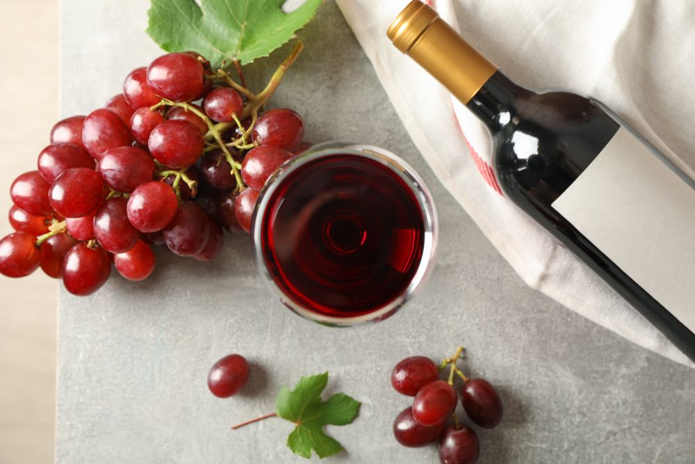 Grape, bottle and glass with wine on grey background, top view