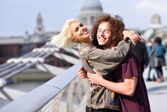 Male and blonde female smiling and hugging on bridge in London