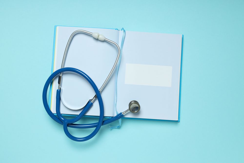 Notepad and stethoscope on blue background, top view