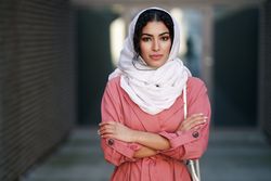 Female in headscarf and pink trench coat standing confidently with her arms crossed