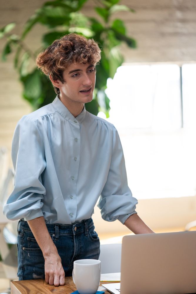 Nonbinary person standing talking at wooden table