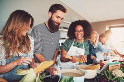 Multi-ethnic group of friends cooking pasta and corn in the kitchen
