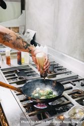 Tattooed arm of chef putting sauce on broccoli in wok 4NpP80