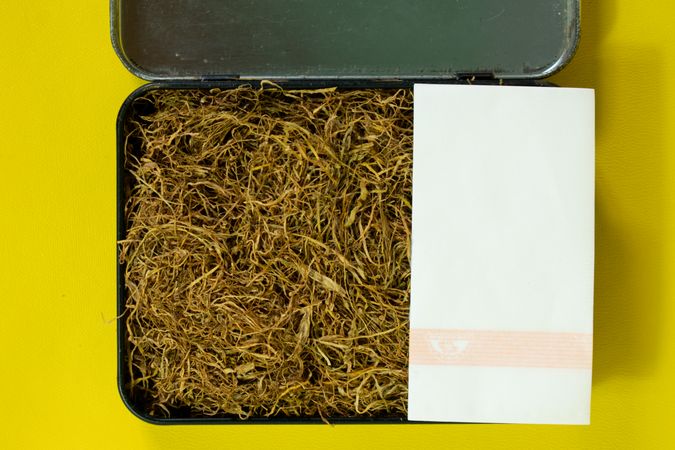 Top view of open box of loose leaf tobacco with rolling papers
