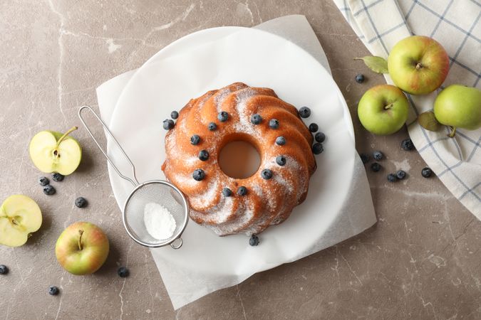 Cake with powder sugar, blueberry and apples on grey background, top view