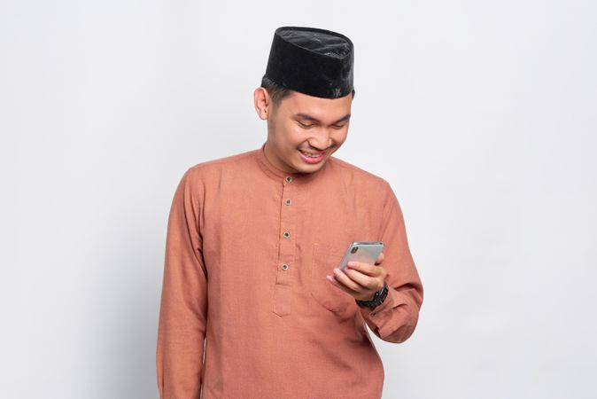Happy Muslim man in kufi hat looking down at smartphone