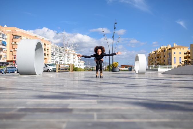 Female with afro and arms spread roller skating outside