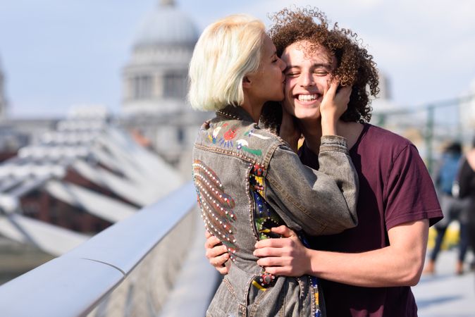 Blonde woman kissing her smiling boyfriend on bridge in London