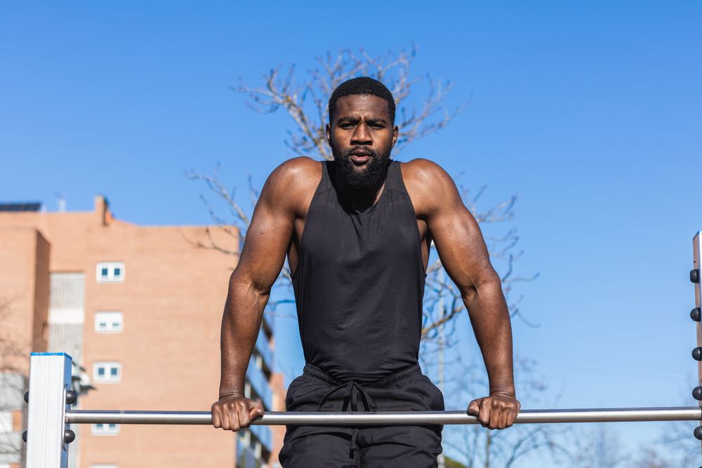 Strong Black sportsman working out on bar in town