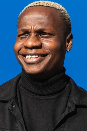 Happy Black guy standing against blue wall in sunlight