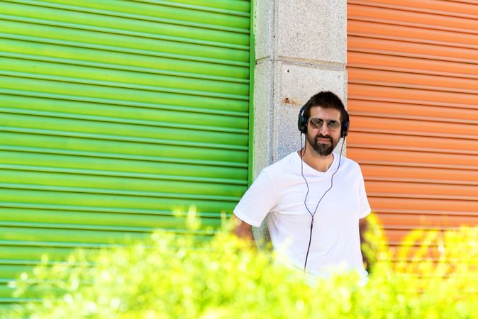 Man in headphones and sunglasses leaning on wall between colorful shutters