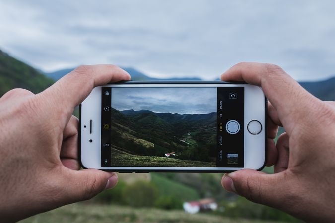 Crop hands taking picture of hilly countryside