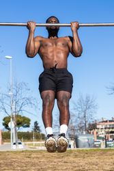 Strong Black sportsman working out on bar in town