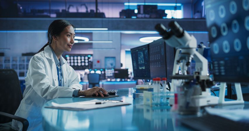 Medical Hospital Research Center Laboratory: Female Asian Neuroscientist Using Desktop Computer With MRI Scans Of Human Brain.
