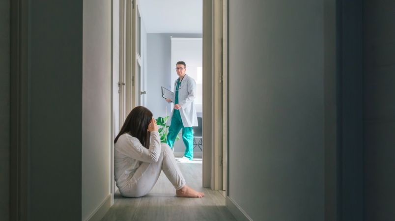 Doctor looking at female patient sitting on floor in hospital