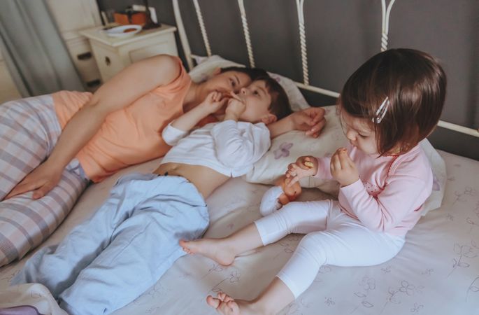 Little girl eating a cookie in bed next to her mother and brother
