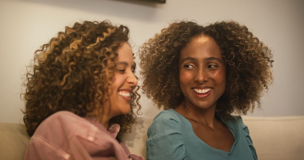 Portrait of Two Brazilian Young Women Using Laptop Computer While Sitting on a Sofa at Home.