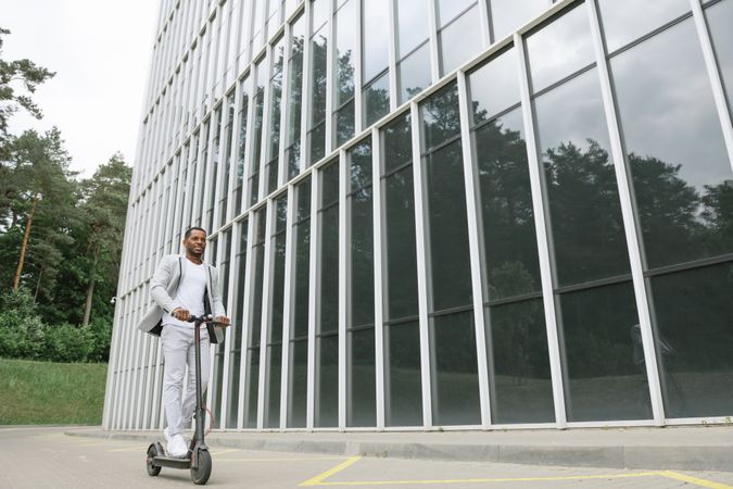 Black man in suit on electric scooter in business center