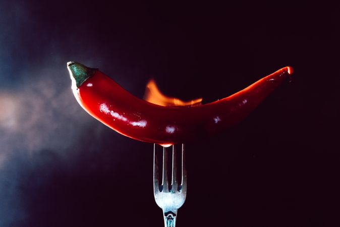 red chili pepper on fire in fork on a dark background