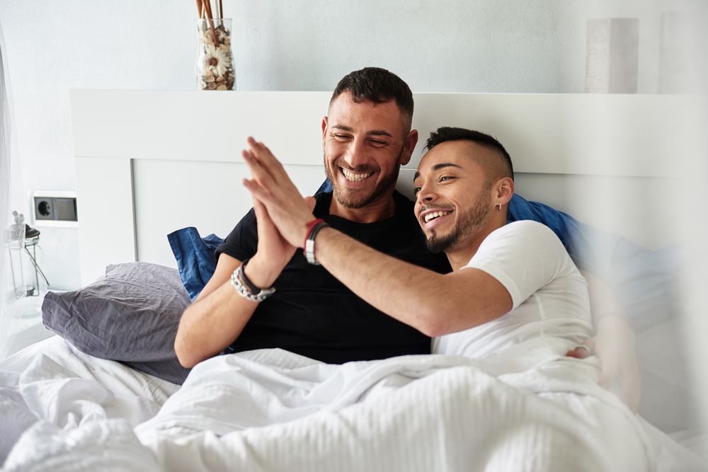 Smiling gay couple hugging on bed