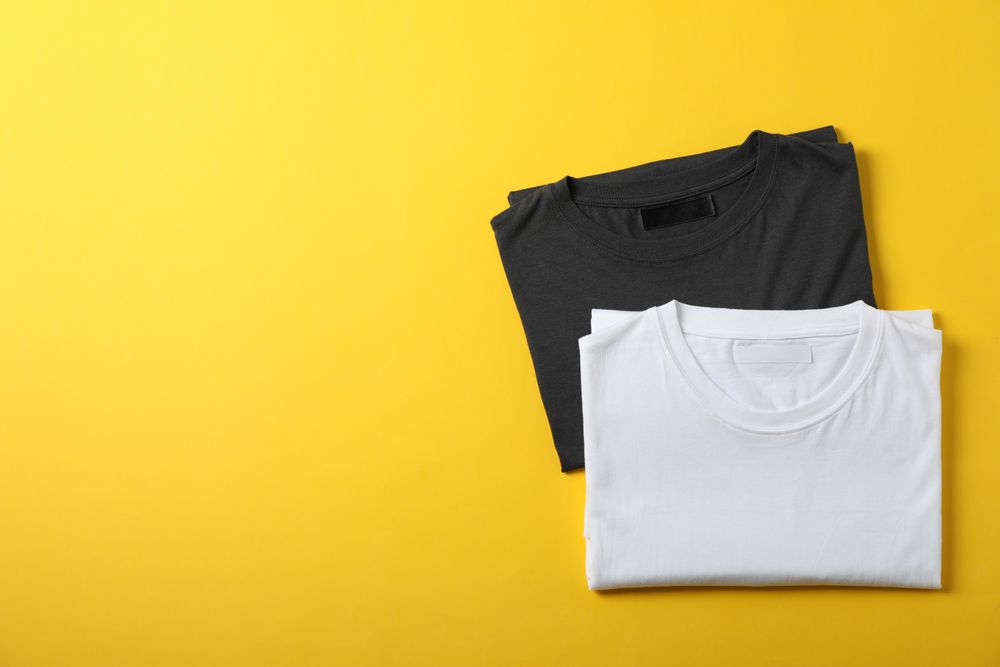 Folded blank t-shirts on yellow background, space for text