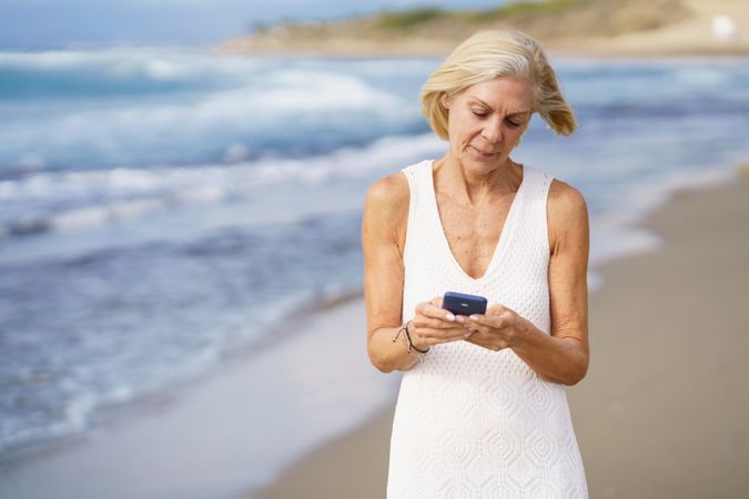 Curious older female using her smart phone on a rocky beach