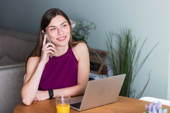 Smiling woman using smartphone and sitting at table with laptop