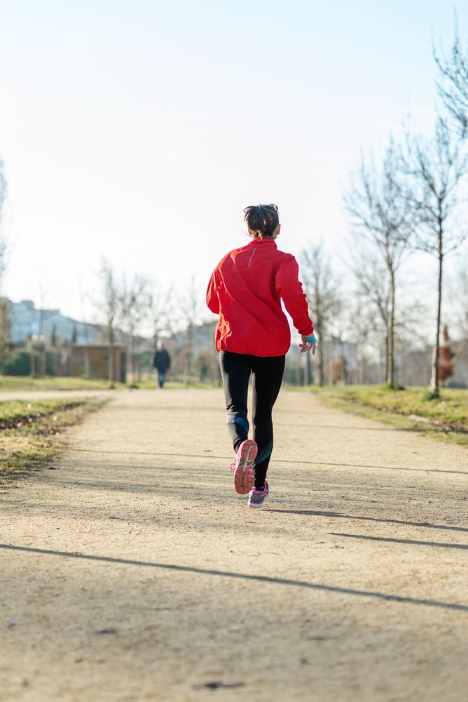 Back of woman running outdoors in park on sunny autumn day