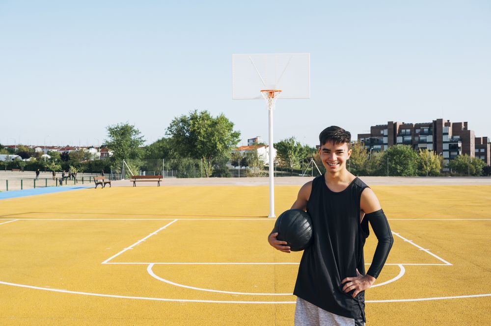 Young man playing on yellow basketball court outdoor.