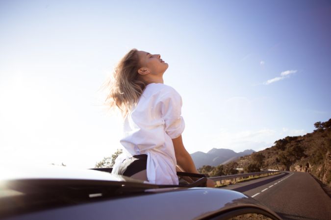 Rearview of relaxed woman standing out of sunroof on sunny day