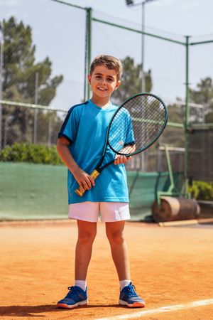 Little boy playing tennis on a dirt court