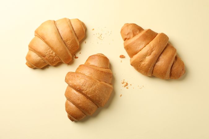 Three baked croissants on beige background, top view